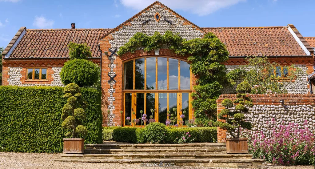 Chaucer Barn's brick-and-flint facade, with tall windows, climbing plants and garden steps.