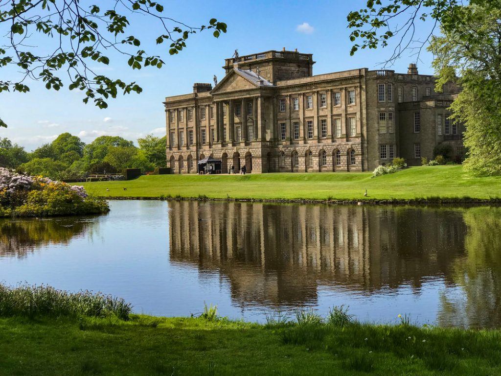 Lyme Park's columned south facade reflected in the lake, framed by trees.